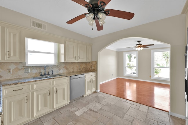 kitchen with sink, light wood-type flooring, stainless steel dishwasher, light stone counters, and decorative backsplash