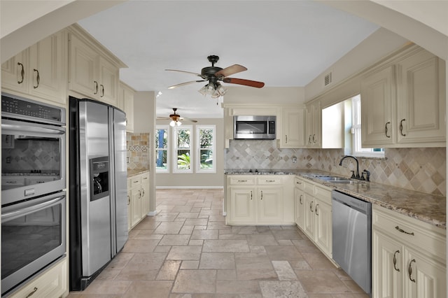 kitchen featuring decorative backsplash, appliances with stainless steel finishes, light stone countertops, cream cabinetry, and sink