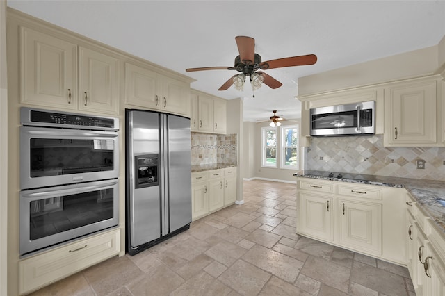 kitchen with tasteful backsplash, ceiling fan, appliances with stainless steel finishes, dark stone countertops, and cream cabinetry