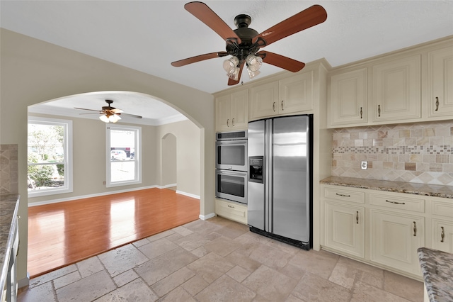 kitchen with cream cabinetry, light hardwood / wood-style flooring, stainless steel appliances, backsplash, and ceiling fan