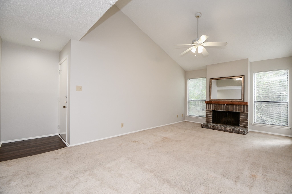 unfurnished living room with ceiling fan, light colored carpet, lofted ceiling, and a brick fireplace