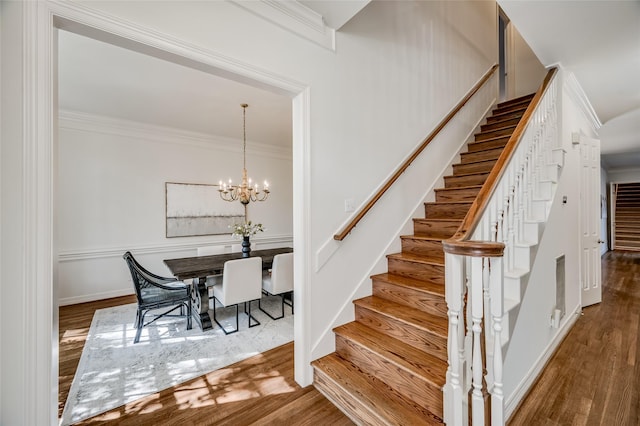 staircase featuring an inviting chandelier, crown molding, and wood-type flooring