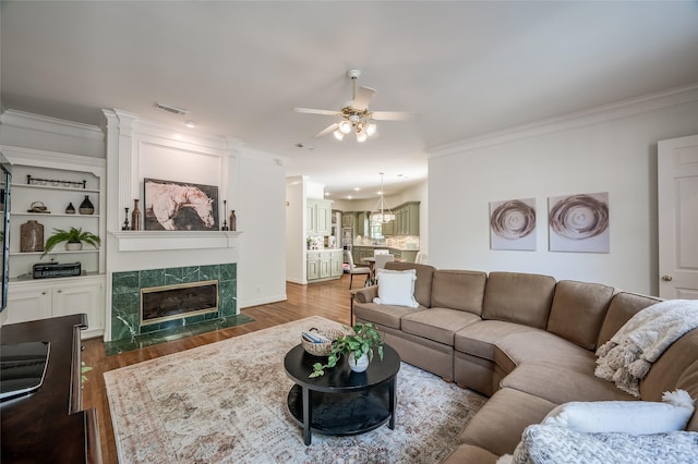 living room with ceiling fan, a premium fireplace, ornamental molding, and built in shelves