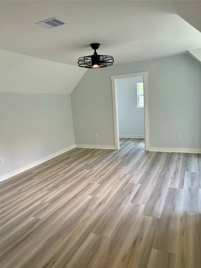 additional living space featuring vaulted ceiling, a textured ceiling, light hardwood / wood-style floors, and ceiling fan