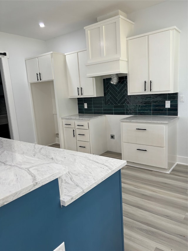 kitchen featuring light stone countertops, decorative backsplash, white cabinets, and light hardwood / wood-style flooring