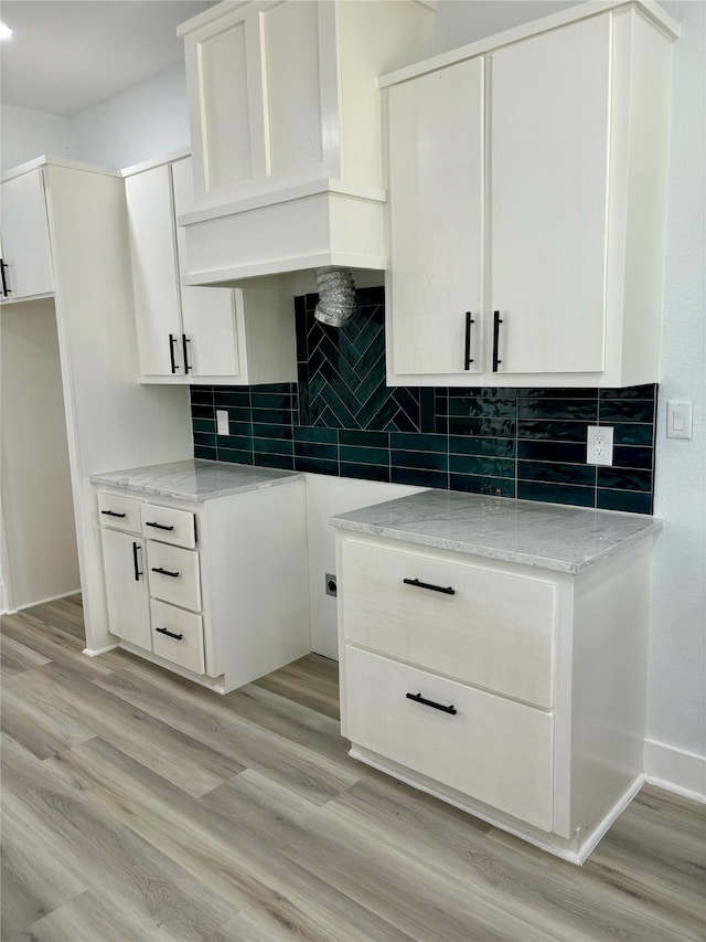 kitchen with light hardwood / wood-style flooring, white cabinetry, custom range hood, and backsplash