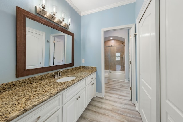 full bathroom featuring crown molding, bath / shower combo with glass door, toilet, vanity, and hardwood / wood-style flooring