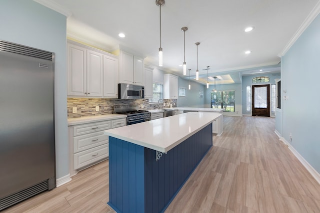 kitchen featuring high end appliances, white cabinets, crown molding, light wood-type flooring, and decorative light fixtures