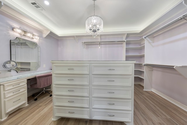 walk in closet with light wood-type flooring, an inviting chandelier, and built in desk