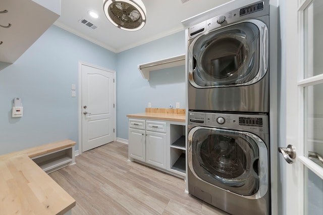 laundry area featuring crown molding, light hardwood / wood-style flooring, cabinets, and stacked washer / drying machine