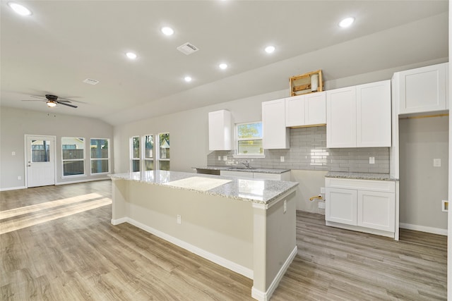 kitchen with lofted ceiling, a kitchen island, white cabinetry, and light hardwood / wood-style floors