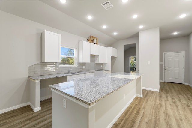 kitchen featuring white cabinets, light stone countertops, light hardwood / wood-style flooring, sink, and a center island