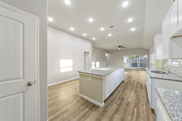 kitchen with white cabinetry, light stone counters, and a kitchen island