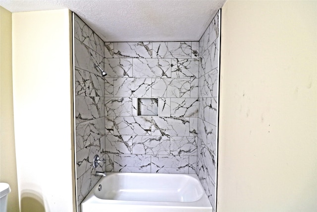 bathroom featuring toilet, a textured ceiling, and tiled shower / bath