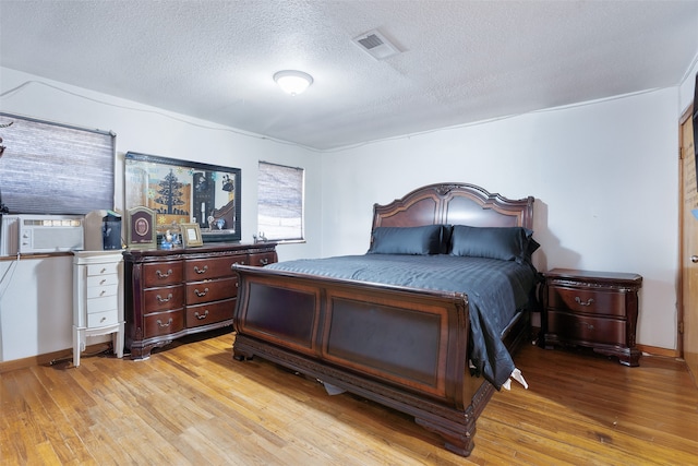 bedroom with light hardwood / wood-style flooring, a textured ceiling, and cooling unit