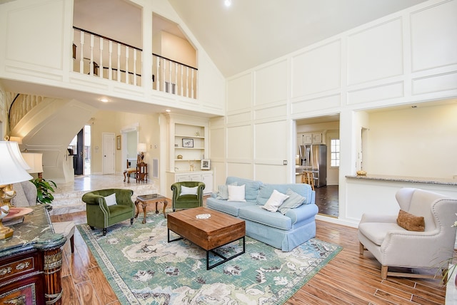 living room featuring high vaulted ceiling, light hardwood / wood-style flooring, and built in shelves