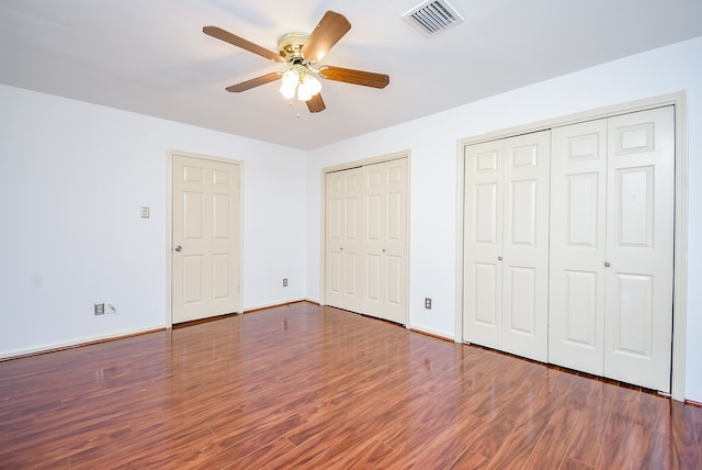 unfurnished bedroom with multiple closets, dark hardwood / wood-style floors, and ceiling fan