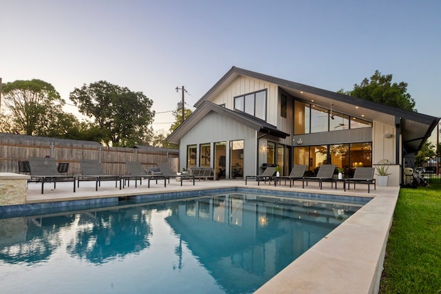 back house at dusk featuring a patio and a fenced in pool