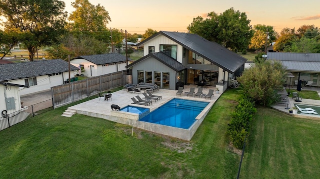 back house at dusk featuring a swimming pool with hot tub, a patio area, and a yard