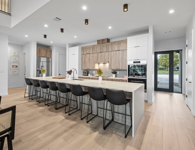 kitchen with a large island with sink, white cabinetry, a kitchen bar, light hardwood / wood-style flooring, and built in refrigerator