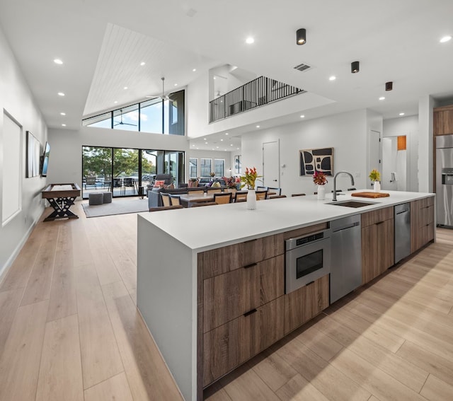 kitchen featuring sink, a large island, a high ceiling, built in appliances, and light hardwood / wood-style flooring