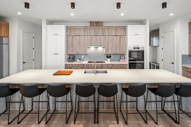 kitchen featuring a large island with sink, stainless steel double oven, a breakfast bar area, and backsplash