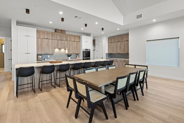 dining room with sink, vaulted ceiling, and light hardwood / wood-style flooring