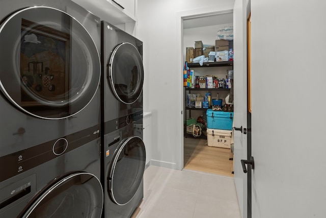 laundry room with stacked washer / dryer, light hardwood / wood-style floors, and cabinets