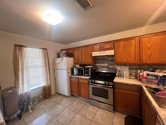 kitchen featuring decorative backsplash, white refrigerator, sink, light tile patterned floors, and gas stove