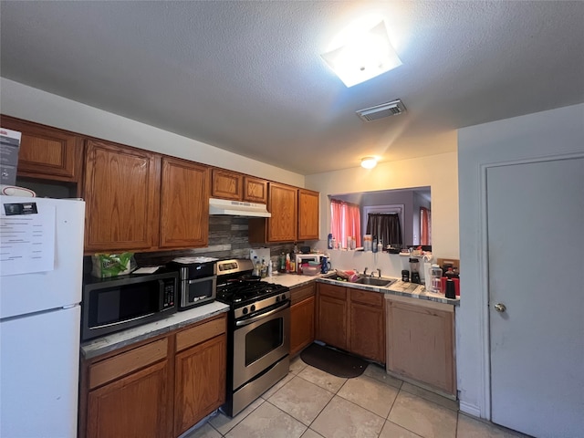 kitchen featuring tasteful backsplash, light tile patterned floors, appliances with stainless steel finishes, a textured ceiling, and sink