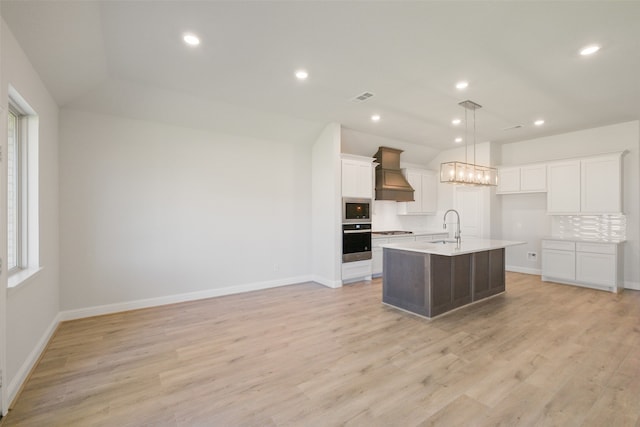 kitchen with appliances with stainless steel finishes, sink, custom range hood, decorative backsplash, and a center island with sink