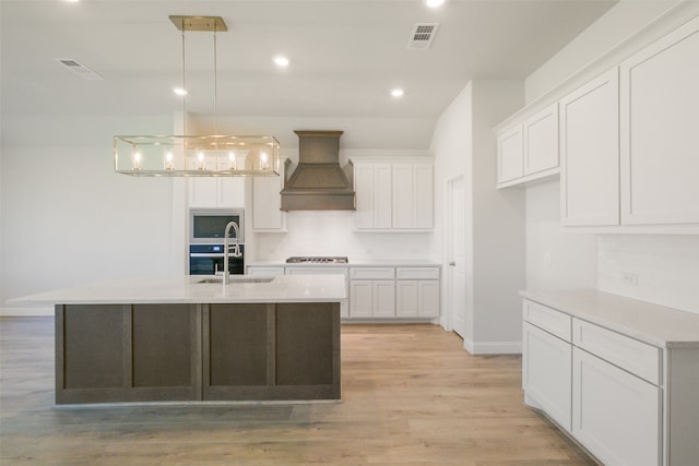 kitchen featuring light wood-type flooring, white cabinetry, pendant lighting, custom exhaust hood, and a center island with sink