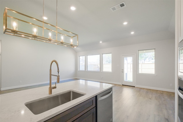 kitchen featuring light stone countertops, appliances with stainless steel finishes, sink, pendant lighting, and light hardwood / wood-style flooring