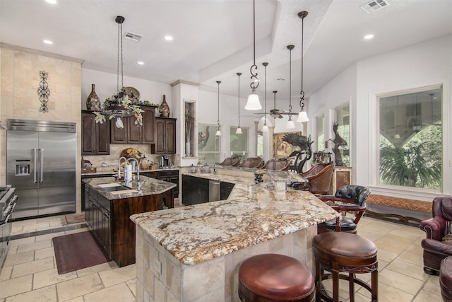 kitchen featuring a kitchen bar, dark brown cabinets, a large island, built in refrigerator, and decorative backsplash