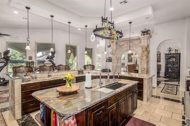 kitchen with a spacious island, sink, decorative light fixtures, light stone counters, and ceiling fan