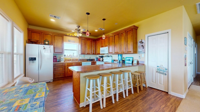 kitchen with white appliances, dark wood-type flooring, kitchen peninsula, and hanging light fixtures