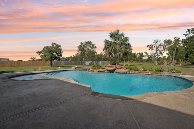 pool at dusk featuring a patio area and an in ground hot tub