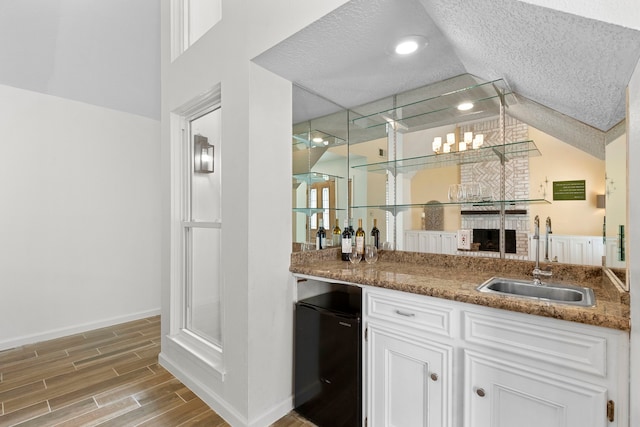 bar with a textured ceiling, white cabinetry, sink, and dark stone counters