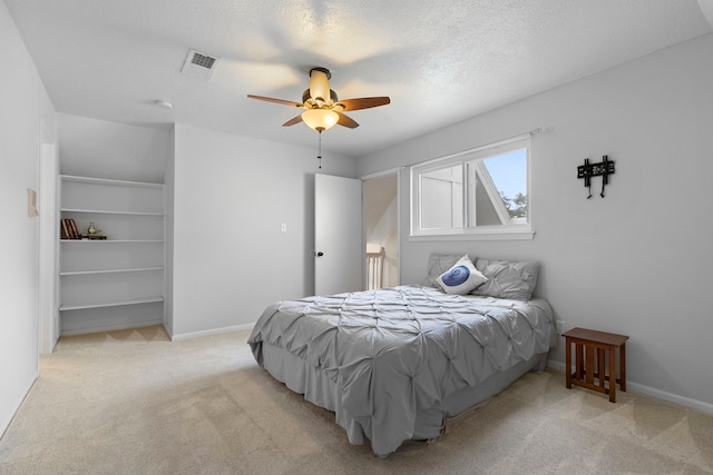 bedroom with ceiling fan, light colored carpet, and a textured ceiling