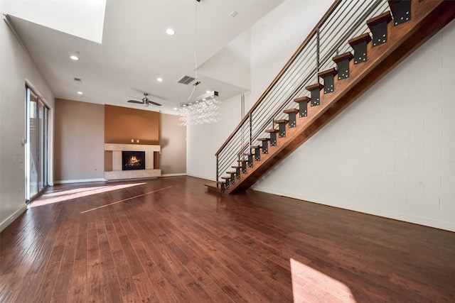 unfurnished living room featuring baseboards, a ceiling fan, stairway, a lit fireplace, and wood-type flooring