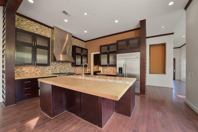 kitchen featuring wall chimney exhaust hood, visible vents, crown molding, built in fridge, and light countertops