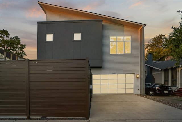 contemporary home with an attached garage, concrete driveway, and fence