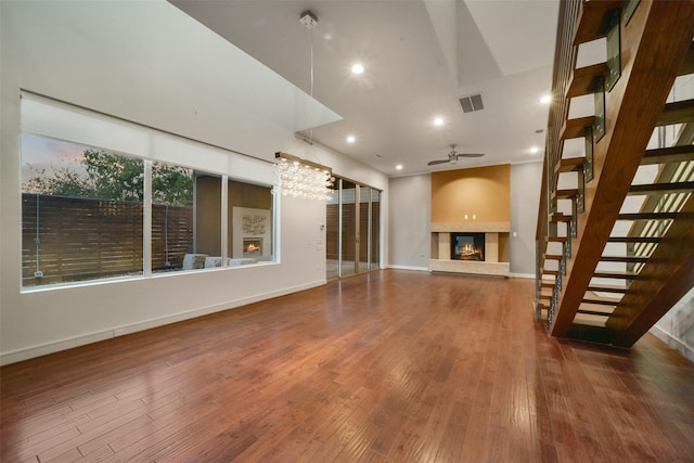 unfurnished living room with ceiling fan with notable chandelier, a glass covered fireplace, wood-type flooring, visible vents, and recessed lighting