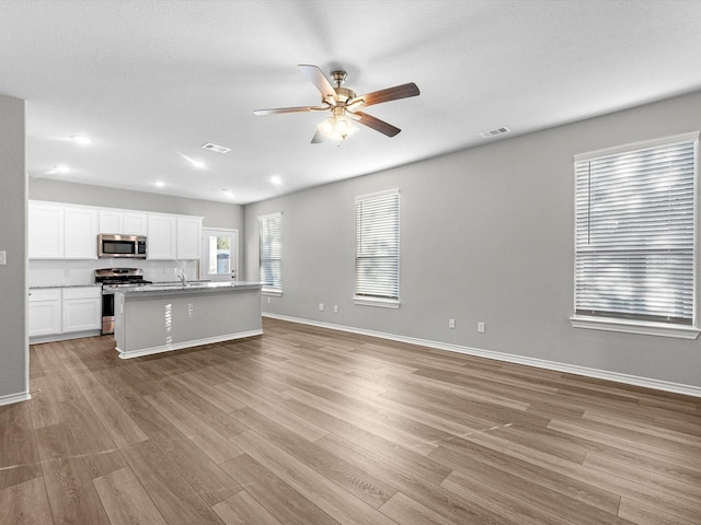 kitchen featuring a kitchen island with sink, stainless steel appliances, light wood-type flooring, ceiling fan, and white cabinetry