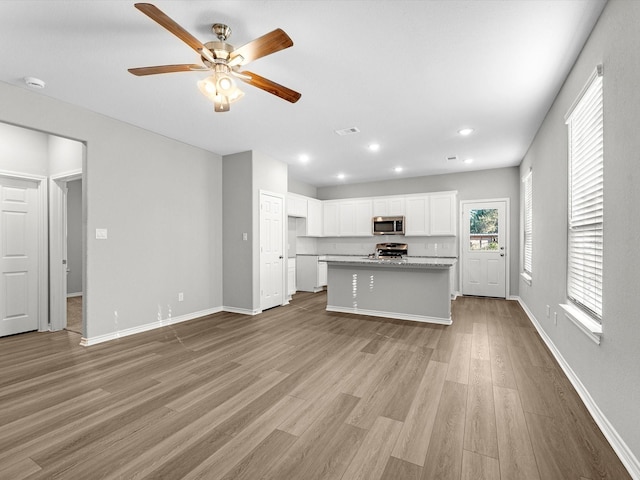 kitchen with a center island with sink, appliances with stainless steel finishes, light wood-type flooring, ceiling fan, and white cabinetry