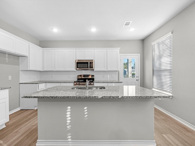 kitchen featuring appliances with stainless steel finishes, light stone countertops, light hardwood / wood-style floors, and an island with sink