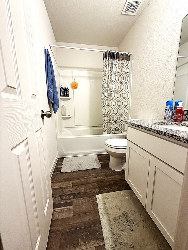 full bathroom with shower / tub combo, a textured ceiling, hardwood / wood-style flooring, toilet, and vanity