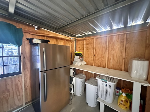 basement with stainless steel refrigerator and wooden walls