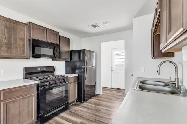 kitchen featuring black appliances, dark brown cabinetry, sink, and light hardwood / wood-style flooring