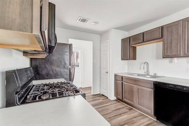 kitchen with black appliances, dark brown cabinetry, sink, and light hardwood / wood-style flooring